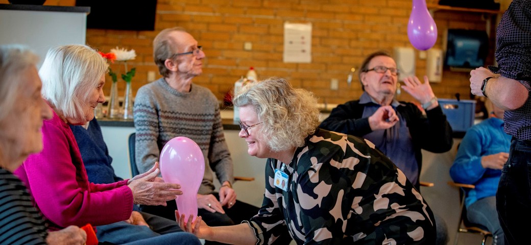 Ballondans i Birke-Bo, hvor kvinde giver en der sidder ned en ballon.