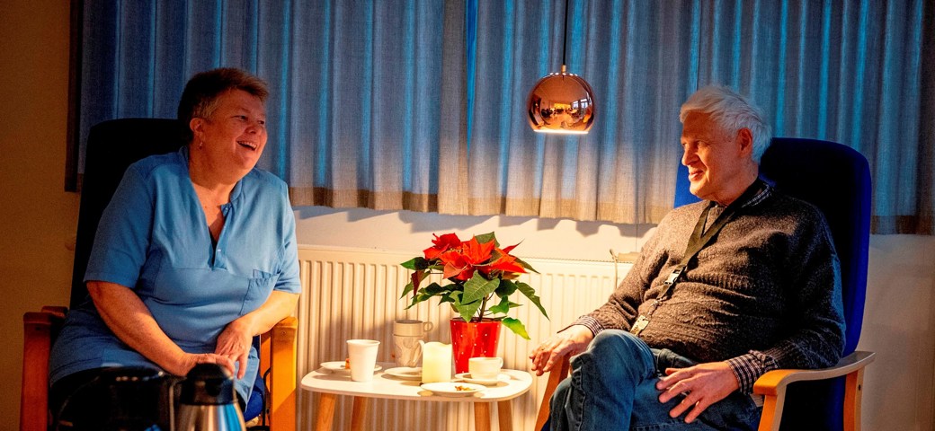 En mand og kvinde sidder i hver dages stol med kaffen imellem sig på daghjemmet på Korinthvej