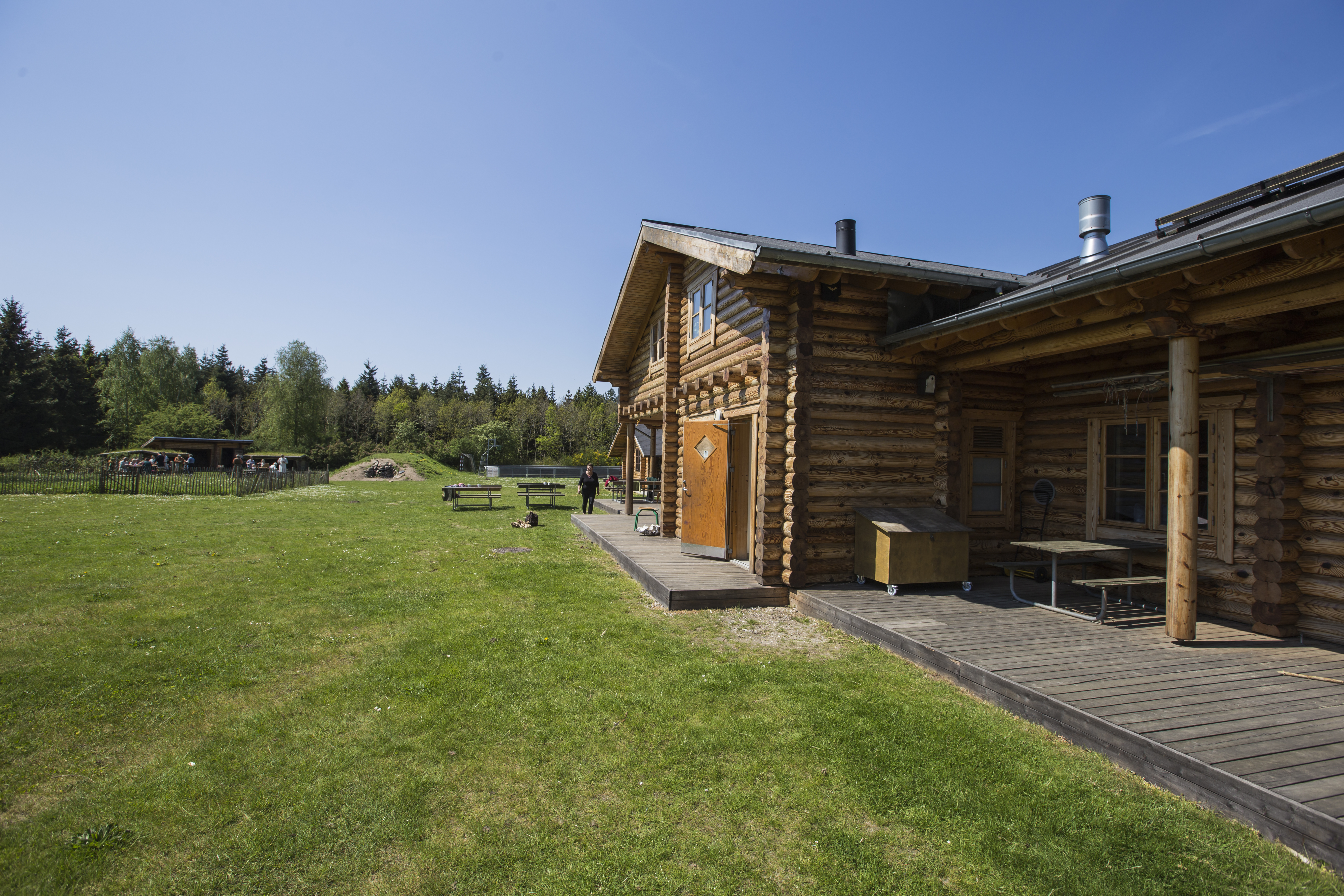 Bjælkehytte på grøn græsplæne og træer i baggrunden