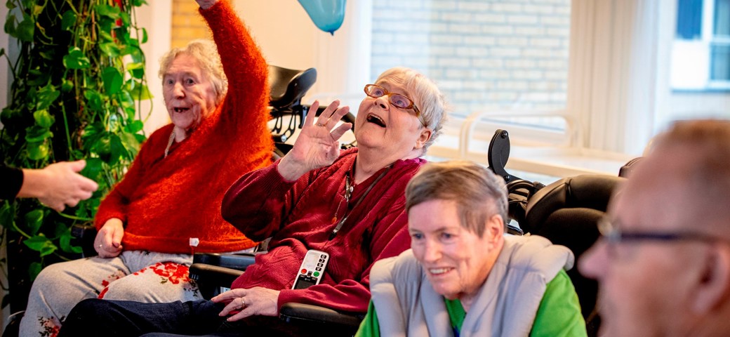 Kvinde, der sidder i kørestol, modtager en flyvende ballon, mens hun smiler op imod den