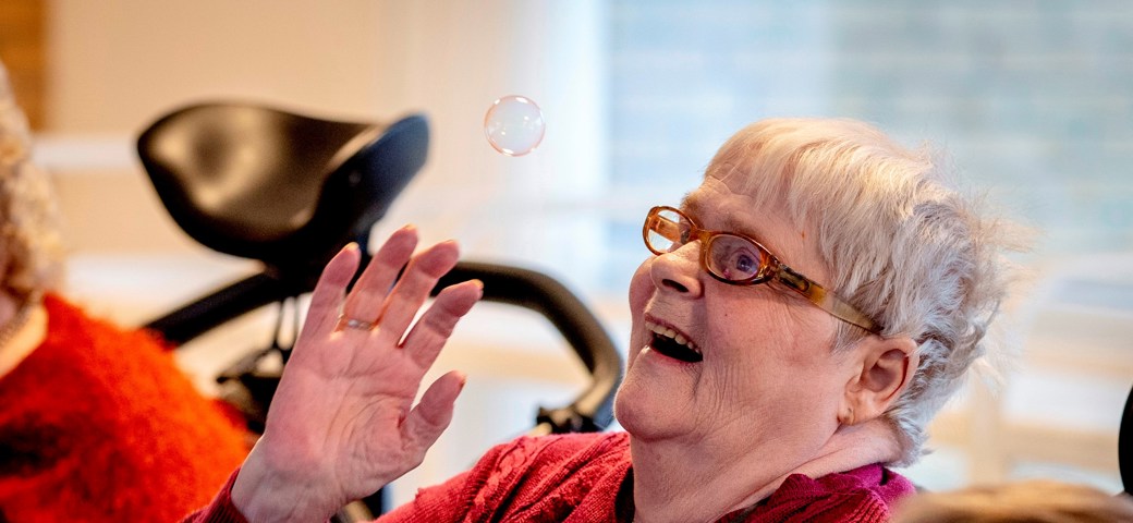 Kvinde, der sidder ned, smiler op imod en sæbebobel.