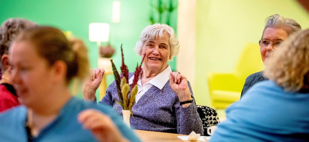 Kvinde smiler, mens hun sidder til fælles arrangement på Bakkegården