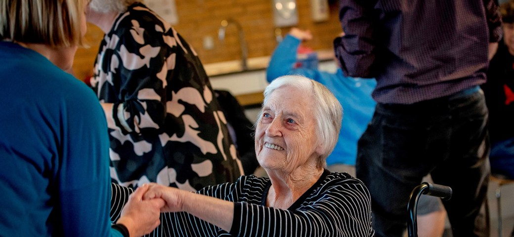Kvinde i kørestol danser med et personale og smiler optil hende
